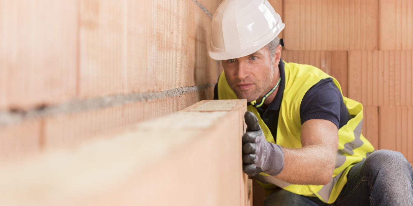 Construction worker checking alignment of mineral-wool filled clay block