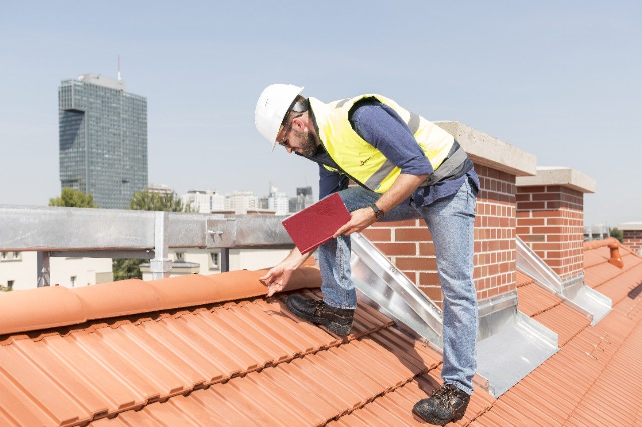 Urban roofers builder standing on roof checking toof tiles wearing hard hat and safety jacket