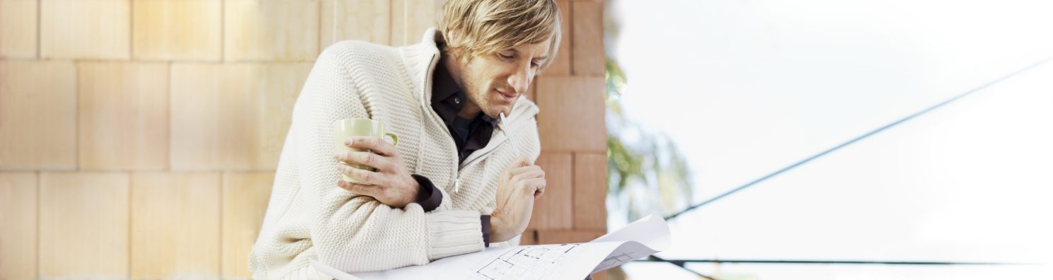 Man with blueprint in unfinished building thinking